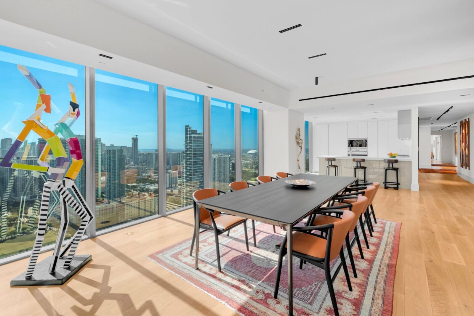 Contemporary dining room with floor-to-ceiling windows, city views, black dining table, and orange accent chairs