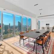 Contemporary dining room with floor-to-ceiling windows, city views, black dining table, and orange accent chairs