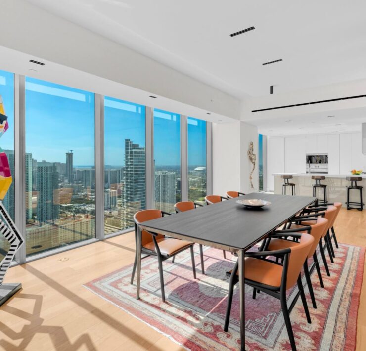 Contemporary dining room with floor-to-ceiling windows, city views, black dining table, and orange accent chairs