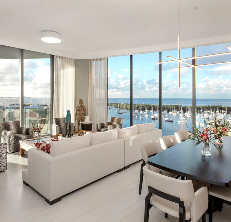 Bright modern living and dining room with marina views, white seating, sculptural chandelier, and black dining table