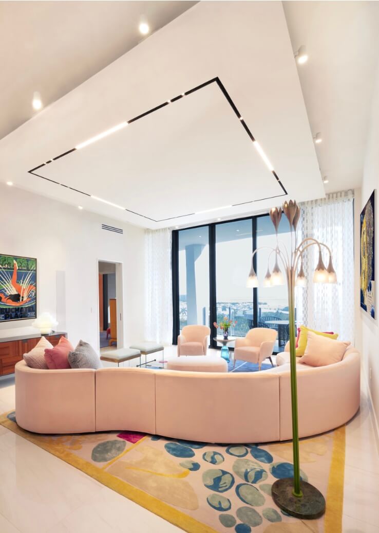 Contemporary living room with curved blush sofa, pastel lounge chairs, sculptural floor lamp, and playful abstract rug