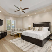 Contemporary bedroom with dark wood furniture, white bedding, neutral seating area, and soft layered textures