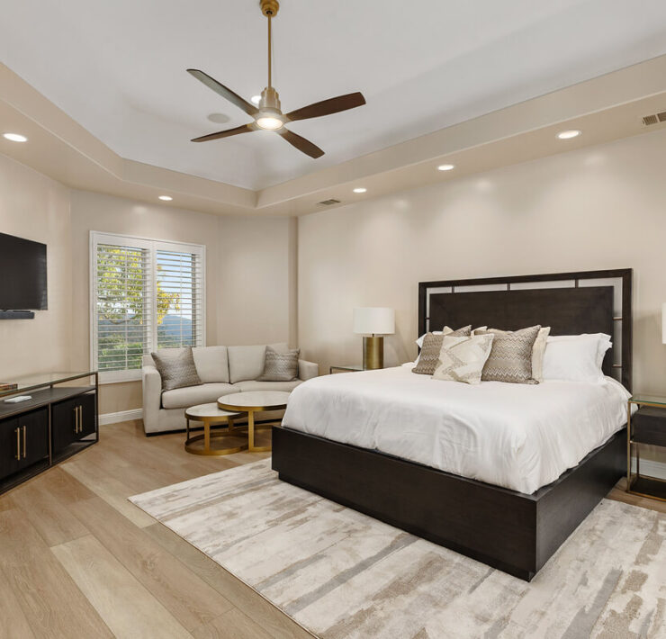 Contemporary bedroom with dark wood furniture, white bedding, neutral seating area, and soft layered textures