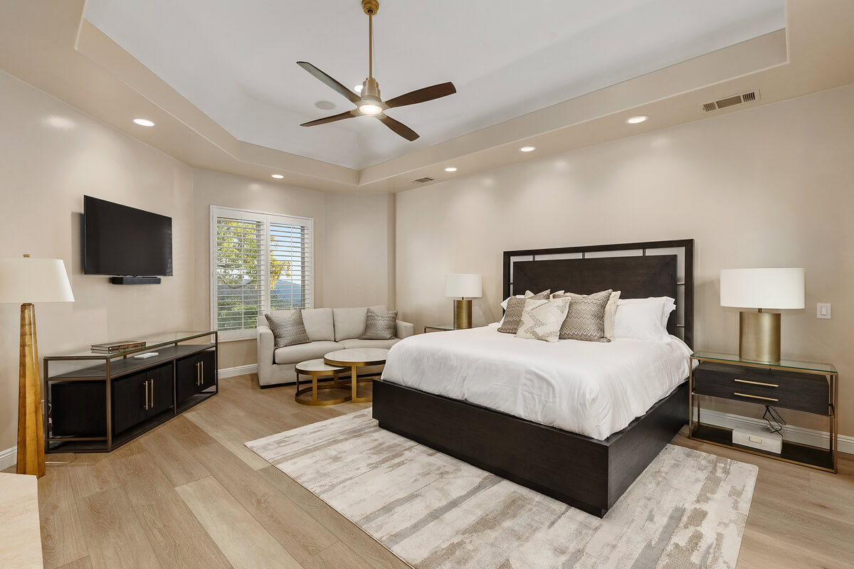 Contemporary bedroom with dark wood furniture, white bedding, neutral seating area, and soft layered textures