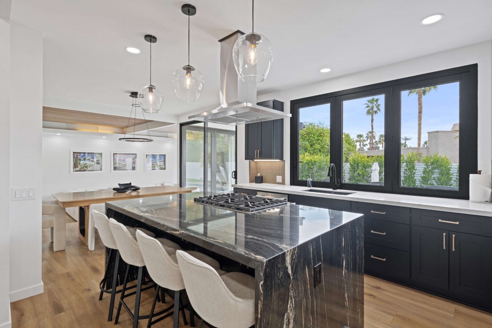 Modern kitchen with dark cabinetry, dramatic stone waterfall island, pendant lights, and large black-framed windows
