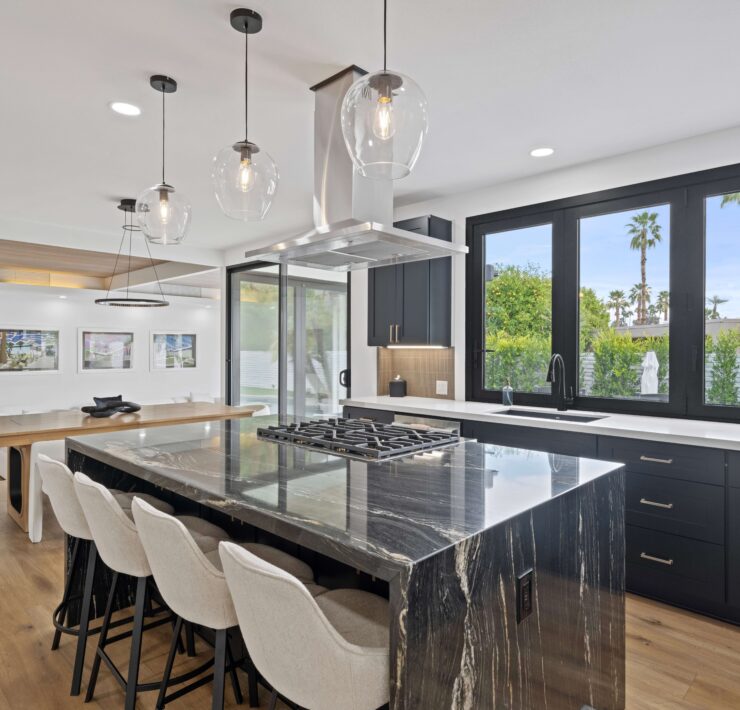 Modern kitchen with dark cabinetry, dramatic stone waterfall island, pendant lights, and large black-framed windows