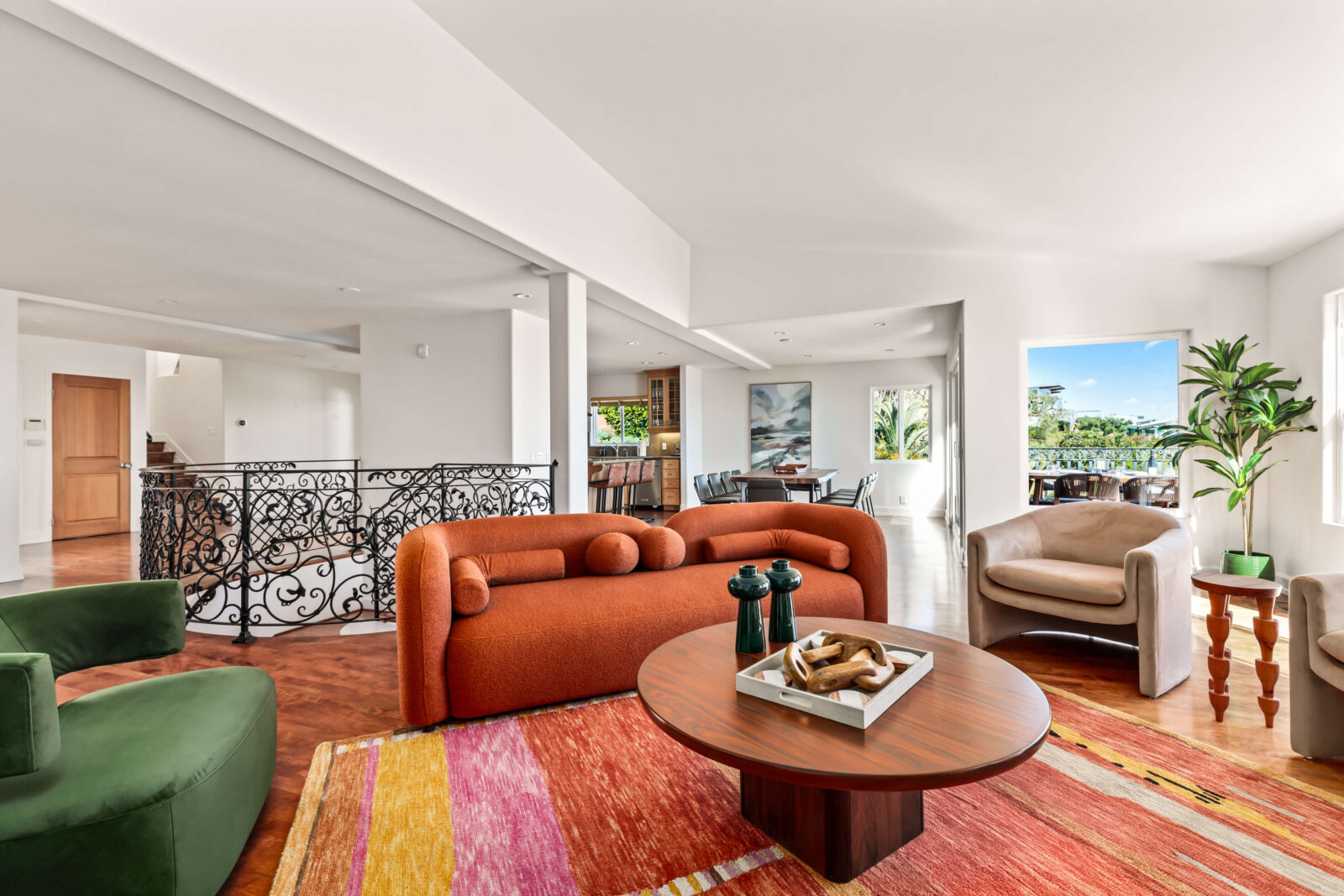 Bright living room with sculptural rust sofa, colorful rug, curved lounge chairs, and ornate black railing