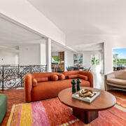 Bright living room with sculptural rust sofa, colorful rug, curved lounge chairs, and ornate black railing