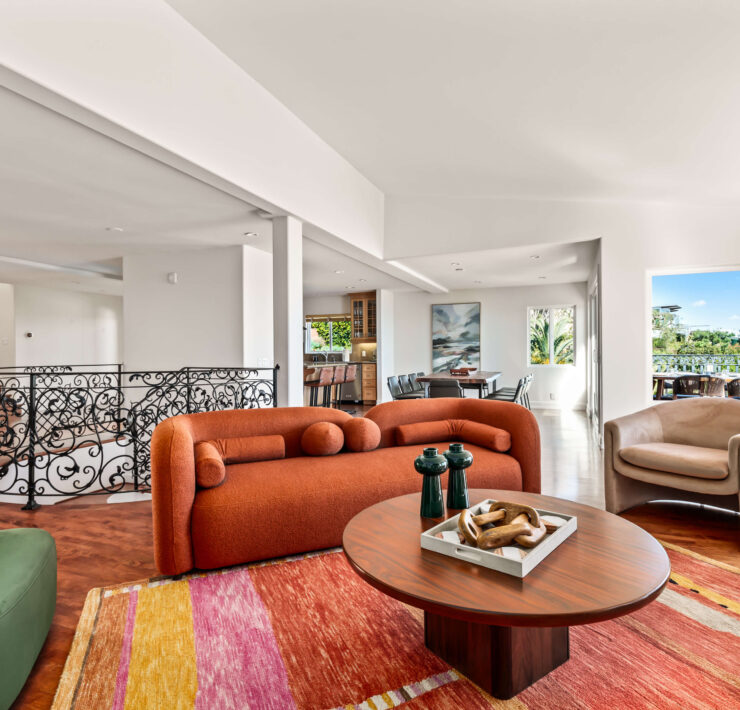 Bright living room with sculptural rust sofa, colorful rug, curved lounge chairs, and ornate black railing