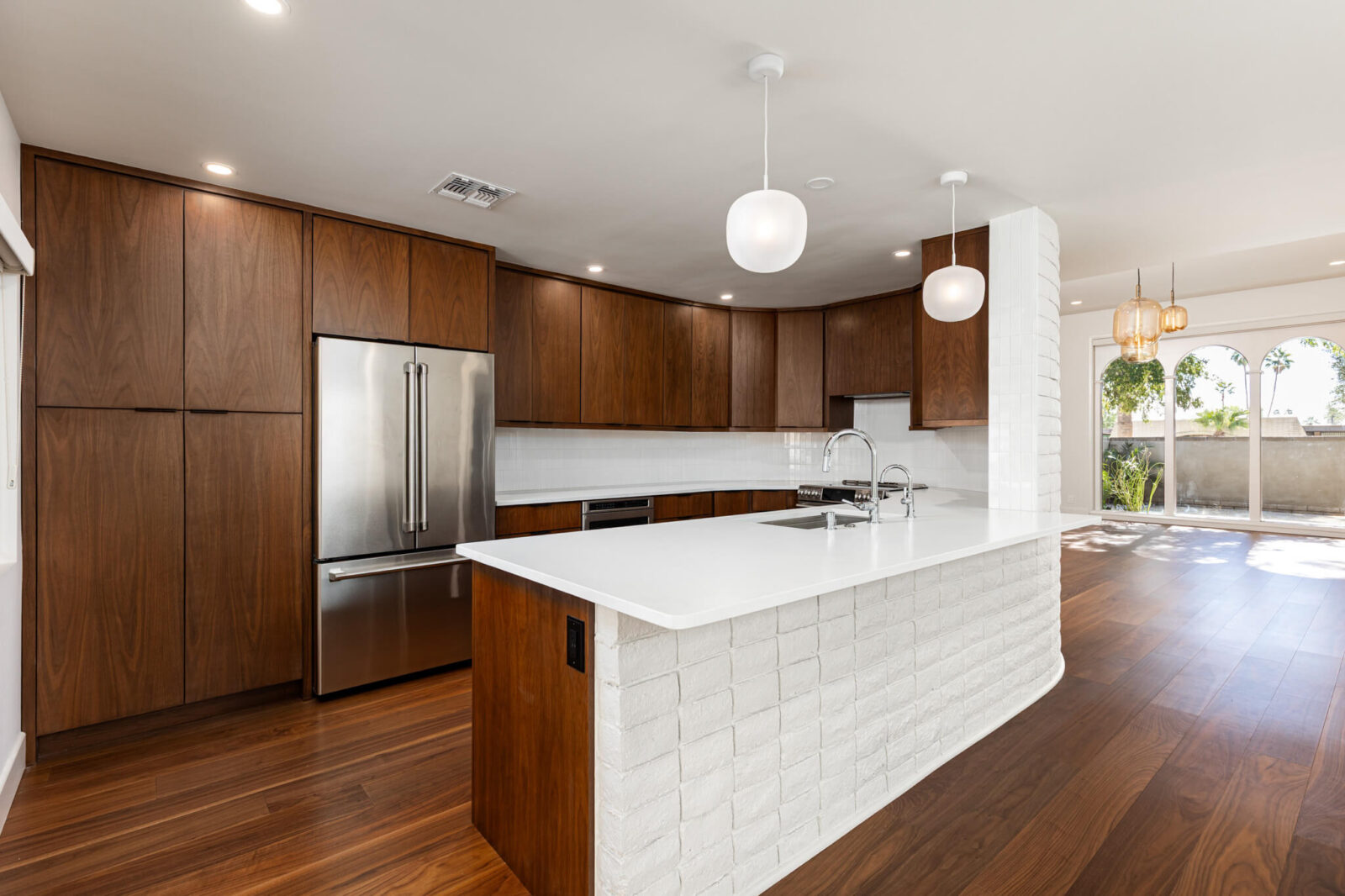 Warm modern kitchen with walnut cabinetry, white island, globe pendants, and rich wood flooring