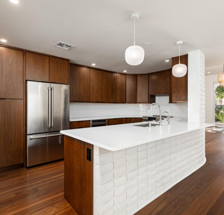 Warm modern kitchen with walnut cabinetry, white island, globe pendants, and rich wood flooring