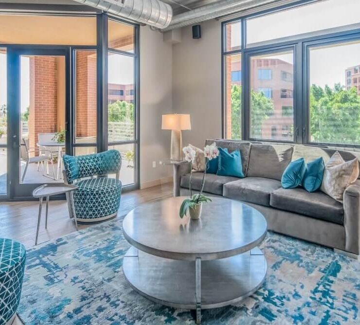 Contemporary loft living room with blue accent chairs, gray sofa, round coffee table, and floor-to-ceiling windows