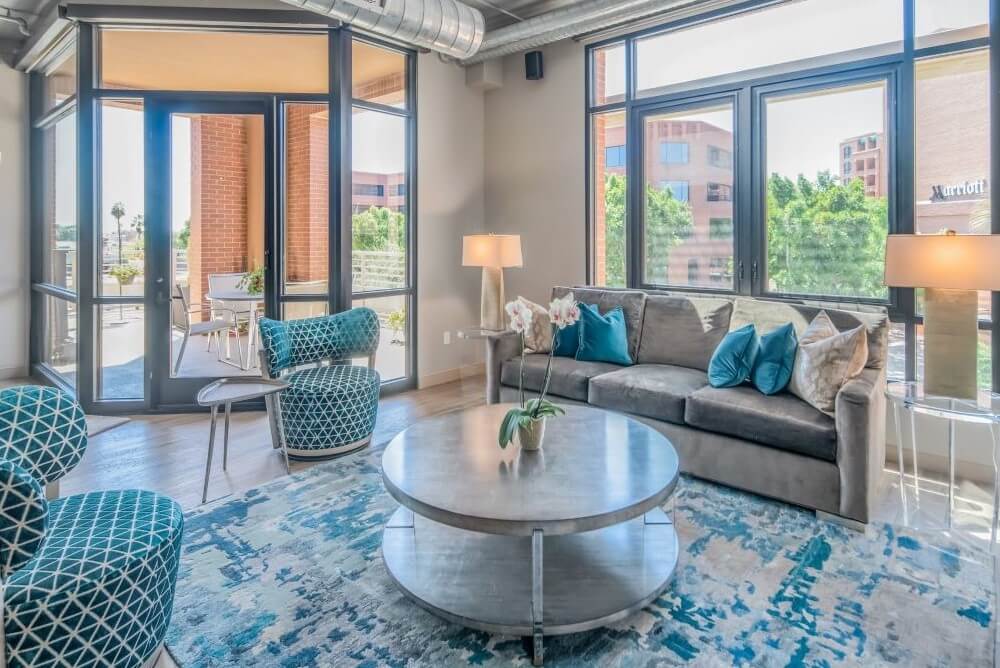 Contemporary loft living room with blue accent chairs, gray sofa, round coffee table, and floor-to-ceiling windows