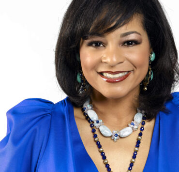 Professional portrait of designer Yvette Craddock wearing a vivid blue dress and statement jewelry