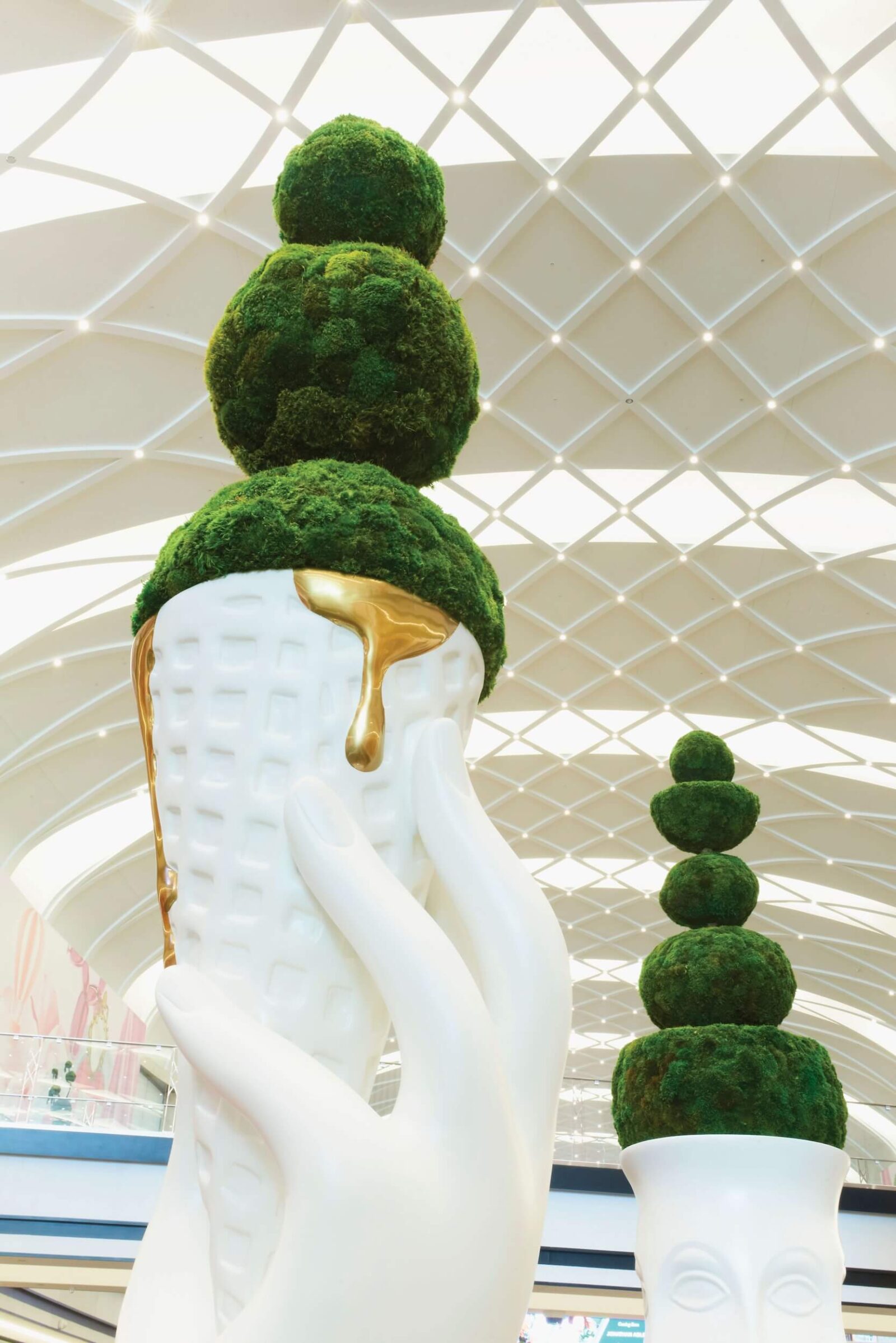 Close-up of artistic moss topiary sculpture with white ceramic planter and gold accent
