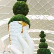 Close-up of artistic moss topiary sculpture with white ceramic planter and gold accent