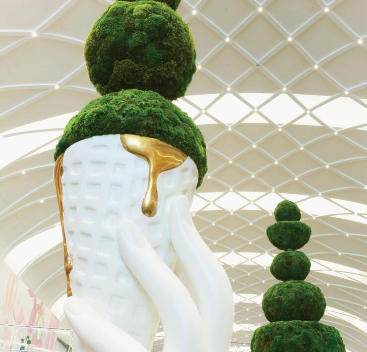 Close-up of artistic moss topiary sculpture with white ceramic planter and gold accent