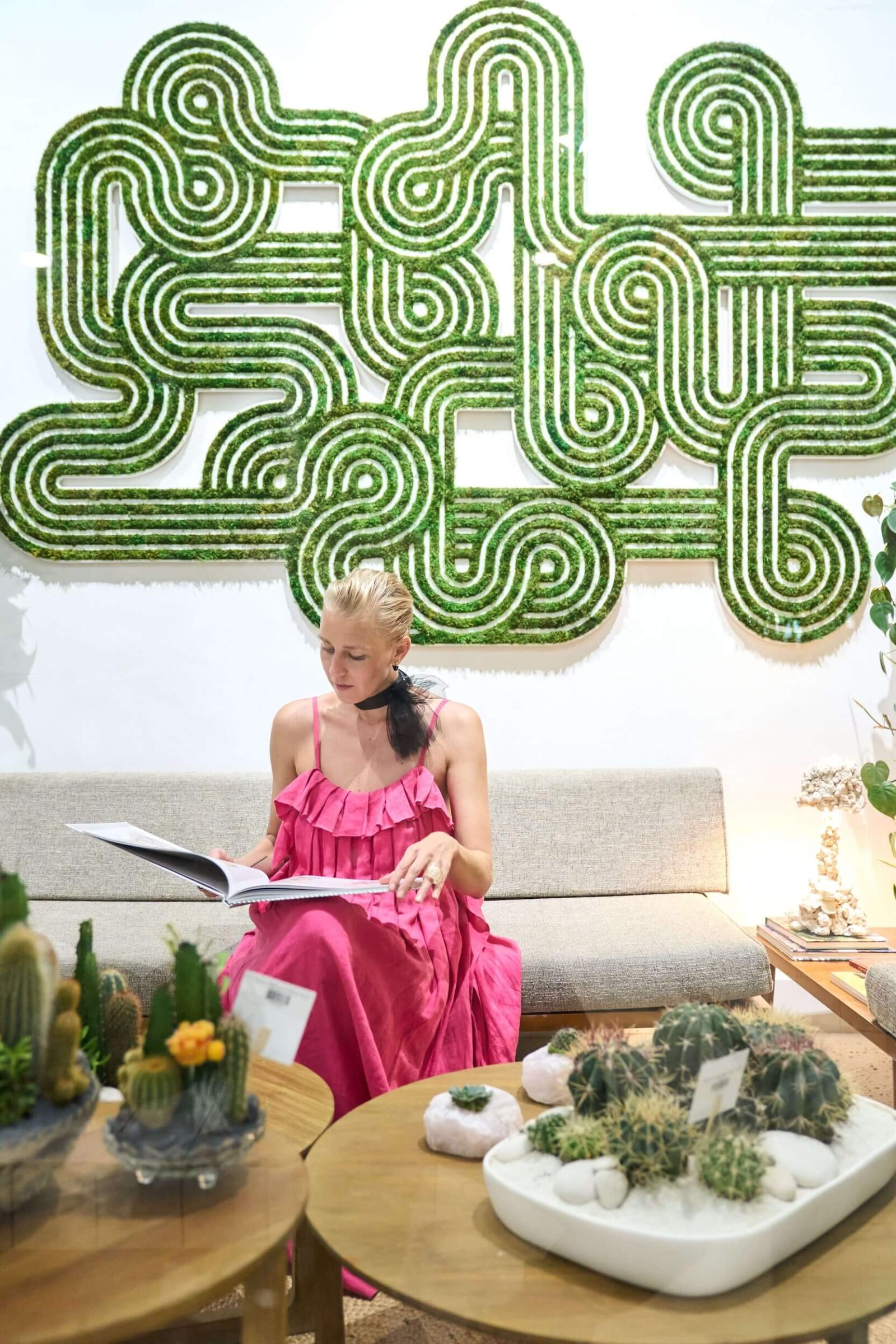Interior designer seated below geometric moss wall art with cactus arrangements