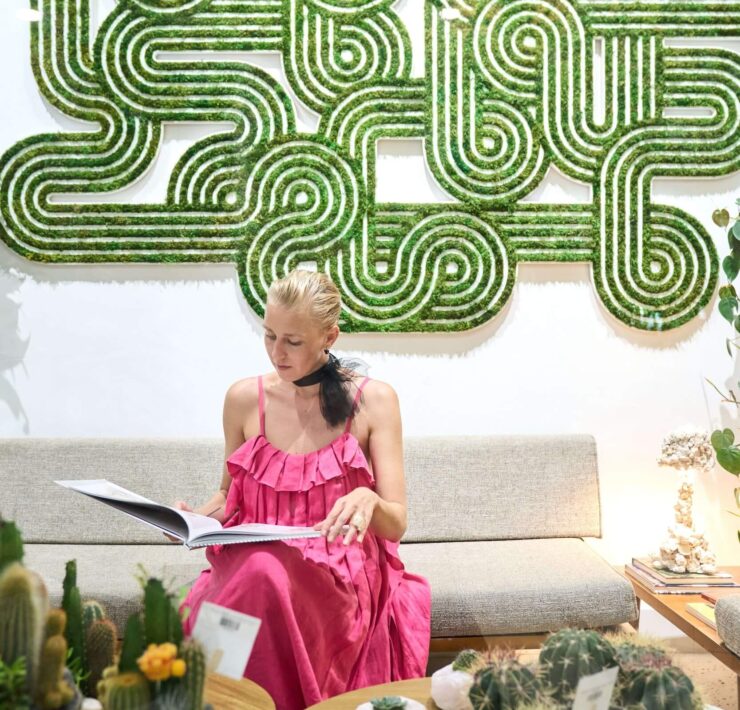 Interior designer seated below geometric moss wall art with cactus arrangements