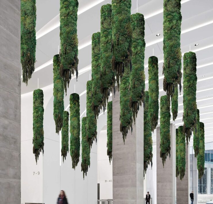 Suspended preserved moss columns hanging from the ceiling in a modern commercial lobby with concrete pillars and minimalist architecture