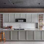 Florense Bistrot kitchen with gray paneled cabinetry, glass-front cabinets, white countertops, and warm wood detailing.