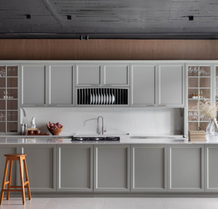 Florense Bistrot kitchen with gray paneled cabinetry, glass-front cabinets, white countertops, and warm wood detailing.