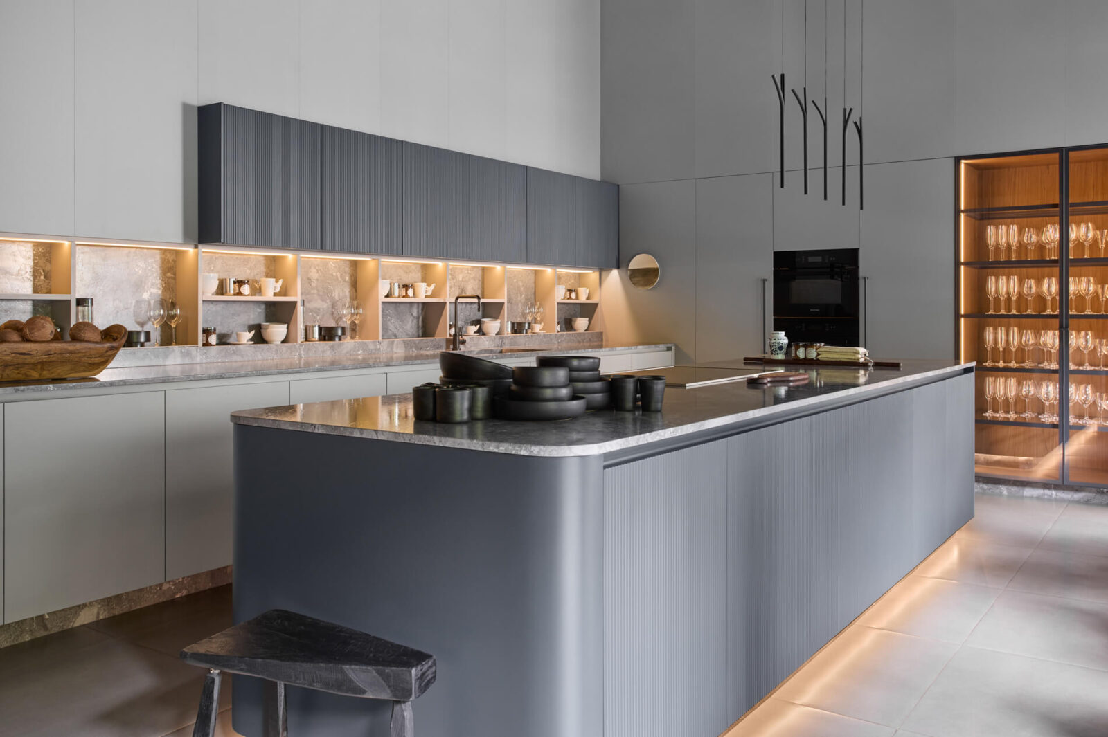 Florense Duna kitchen with gray fluted cabinetry, illuminated open shelving, stone countertops, and modern glass display storage.