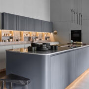 Florense Duna kitchen with gray fluted cabinetry, illuminated open shelving, stone countertops, and modern glass display storage.