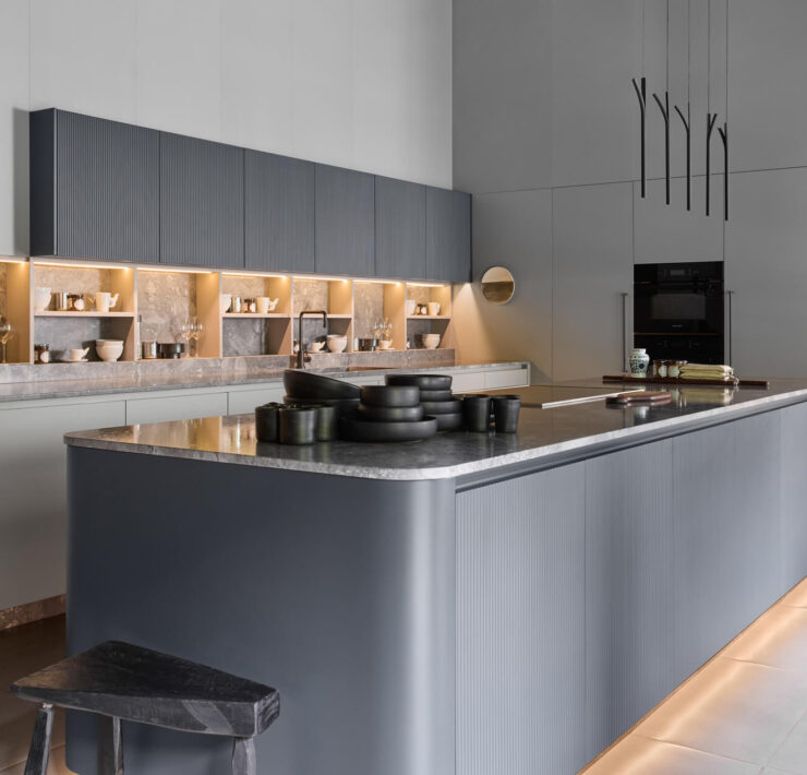 Florense Duna kitchen with gray fluted cabinetry, illuminated open shelving, stone countertops, and modern glass display storage.