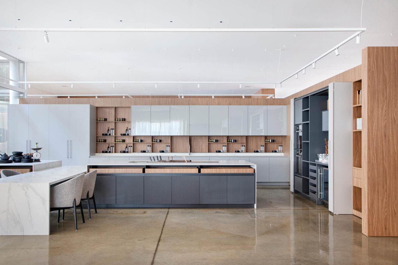 Florense Moderna Kitchen with white and wood cabinetry, large island, integrated appliances, open shelving, and polished concrete floors.