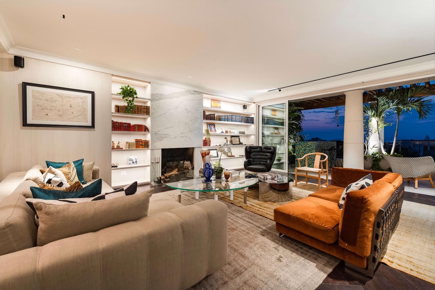 Trazzo luxury living room lighting design with fireplace lighting, illuminated shelving, recessed lighting, and warm indoor-outdoor ambiance.