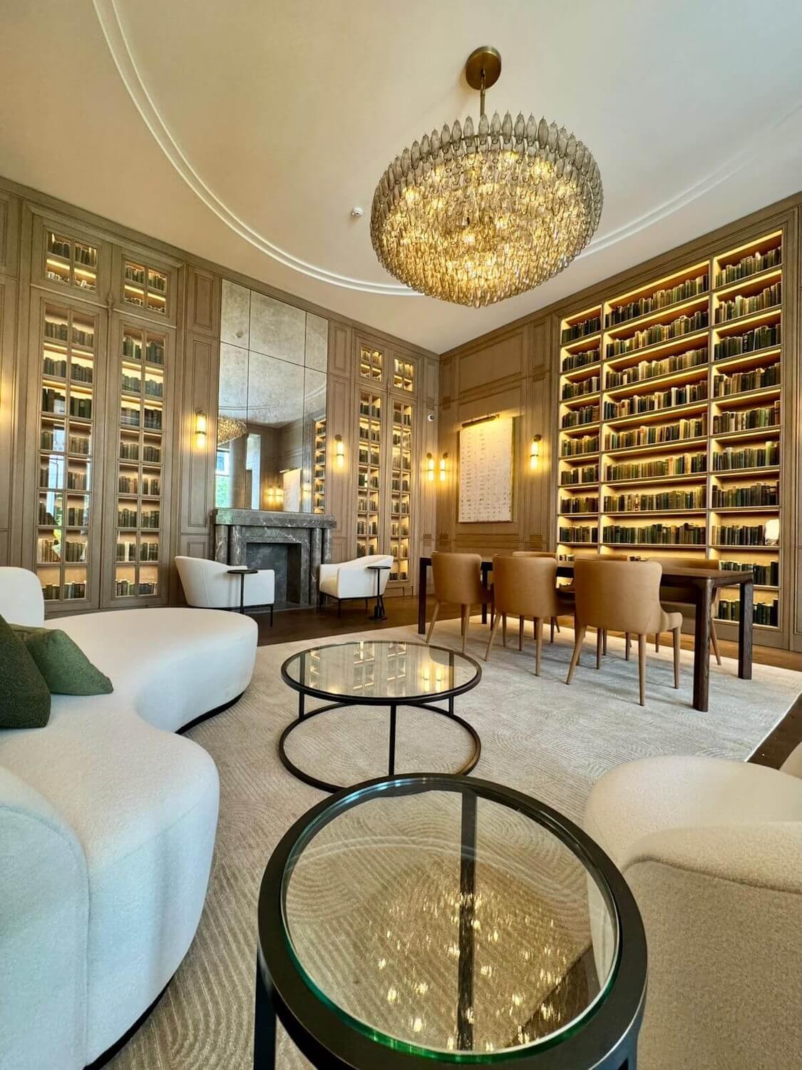 Trazzo luxury library lighting design with illuminated bookshelves, chandelier, wall sconces, fireplace, and warm architectural lighting.