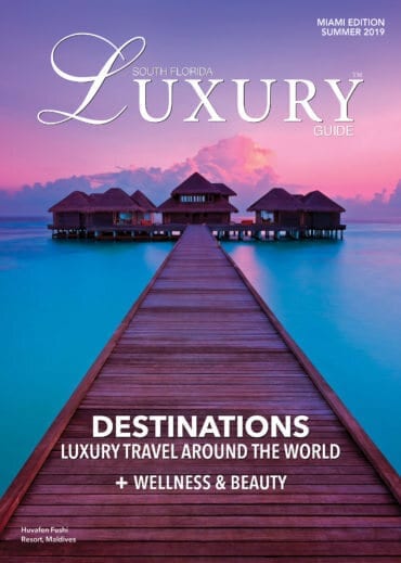 Luxury Guide Cover Summer 2019 South Florida Luxury Guide Miami Summer 2019 cover featuring a wooden boardwalk leading to overwater villas beneath a pink and purple sunset.